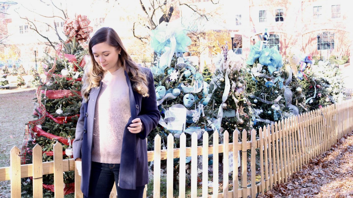 Katie in navy coat in front of christmas trees